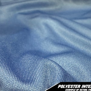 May include: Close-up of a light blue polyester interlock fabric. The fabric is textured and has a slight sheen. The image includes the text "POLYESTER INTERLOCK EXAMPLE OF ACTUAL FABRIC" in the bottom right corner.