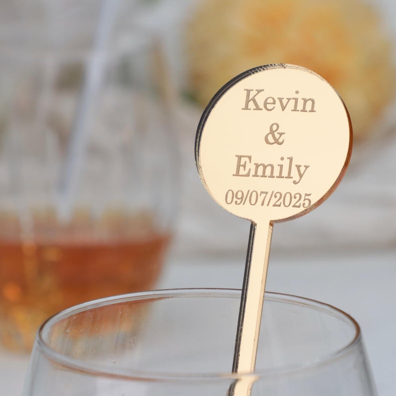 May include: Gold-colored acrylic drink stirrer with a round topper. The topper has the text "Kevin & Emily 09/07/2025" engraved on it.