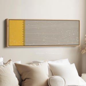 May include: A framed rectangular artwork with a wooden surround. The art displays a yellow section on the left and black horizontal lines on a cream backdrop. The text "Atelier Printworks." is visible at the bottom.