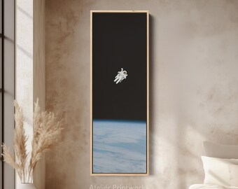 May include: A framed print featuring an astronaut floating in space. The artwork shows a black sky above a blue and white planet. The print is in a rectangular, vertical format with a light wood frame. The text "Atelier Printworks" is at the bottom.