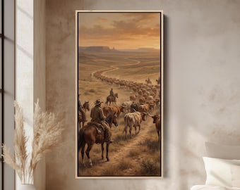 May include: A framed landscape painting depicts a cattle drive in a desert setting. Cowboys on horseback herd cattle along a winding dirt road. The sky is a warm blend of orange and yellow hues, suggesting either sunrise or sunset.