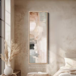 Può includere: Stampa artistica astratta verticale e rettangolare. L'opera presenta una miscela di colori neutri, beige, marrone, grigio e bianco, con motivi simili a pennellate. La stampa è incorniciata in una cornice di legno chiaro. Il testo "Atelier Printworks" è in basso.