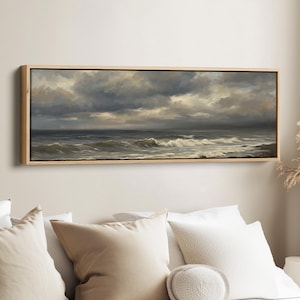 May include: A rectangular framed painting of a stormy sea. The artwork shows a dark, cloudy sky above choppy waves. The painting is in a light-coloured wooden frame, suitable for wall decor, and would suit a living room.