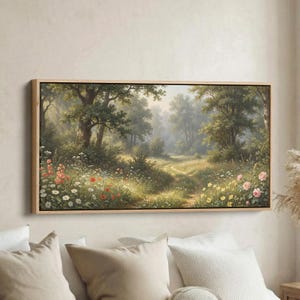 May include: A framed landscape painting depicts a sunlit forest scene. The artwork features a winding path, lush greenery, and a variety of wildflowers in shades of red, pink, yellow, and white. The painting is encased in a light-colored wooden frame.