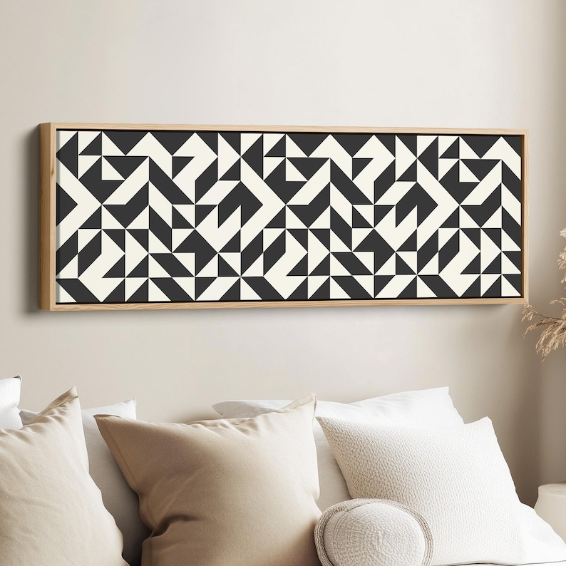 Puede incluir: Una pieza de arte mural rectangular que presenta un patr&oacute;n geom&eacute;trico repetitivo de tri&aacute;ngulos y cuadrados en negro y blanco roto. La obra est&aacute; encerrada en un marco de madera clara, mostrando un dise&ntilde;o abstracto de alto contraste.