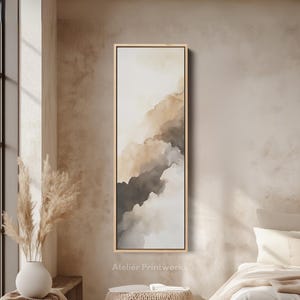 May include: Vertical rectangular art print with an abstract design. The artwork uses a watercolour style with beige, brown, and grey tones, evoking clouds or mountains. It's framed in a light wood frame. The text "Atelier Printworks" is visible on the print.