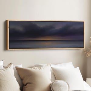 May include: A rectangular landscape painting depicts a moody seascape with a dark, cloudy sky and a hint of golden light on the horizon. The artwork is framed in a natural wood frame, adding a touch of warmth to the scene.