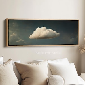 May include: A rectangular framed print of a cloud in a dark sky. The cloud is white and fluffy, set against a backdrop of grey and blue. The frame is made of light-coloured wood. Text at the bottom reads "Atelier Printworks."