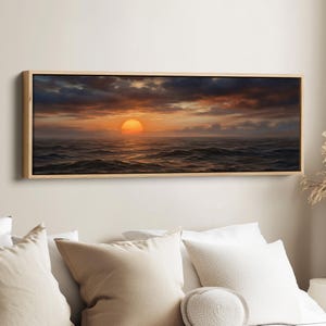 Könnte beinhalten: Gerahmter Leinwanddruck, der einen Sonnenuntergang über einem dunklen Ozean zeigt. Die Sonne ist eine leuchtend orangefarbene Kugel, und der Himmel ist mit dunklen Wolken gefüllt. Die Wellen sind unruhig, und die Gesamtstimmung ist dramatisch. Der Rahmen ist aus hellem Holz.
