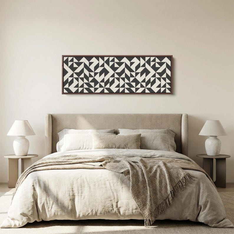 Puede incluir: Una pieza de arte mural rectangular con un patr&oacute;n geom&eacute;trico repetitivo de tri&aacute;ngulos y cuadrados en negro y blanco roto, encerrada en un marco de madera fino de color marr&oacute;n oscuro, montada horizontalmente sobre una pared beige claro.