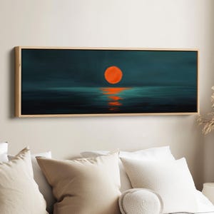 May include: A panoramic rectangular wall art piece featuring a dark teal and navy blue seascape at night. A vibrant, solid orange circular sun is positioned in the centre, casting a shimmering, broken orange reflection across the dark water surface.