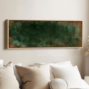 May include: An abstract rectangular artwork with a dark green and brown textured design, framed in natural wood. The piece is mounted on a wall above a bed with white pillows. The text "Atelier Printworks" is visible.