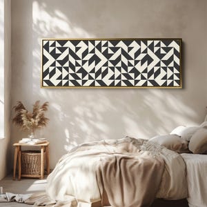 Puede incluir: Una pieza de arte mural rectangular que presenta un patr&oacute;n geom&eacute;trico repetitivo de tri&aacute;ngulos y cuadrados en negro y blanco roto. La obra est&aacute; encerrada en un marco fino de metal dorado, mostrando un dise&ntilde;o sim&eacute;trico de alto contraste.