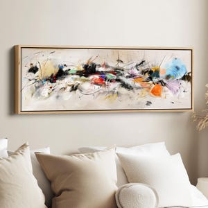 Könnte beinhalten: Abstrakter Kunstdruck auf Leinwand in einem rechteckigen Holzrahmen. Das Kunstwerk zeigt eine Mischung aus Farben, darunter Schwarz, Rot, Orange, Gelb und Blau, mit dynamischen Pinselstrichen und Spritzern auf neutralem Hintergrund. Das Gemälde wird über einem Bett ausgestellt.