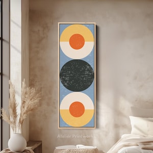 May include: Vertical framed art print featuring three stacked circles in a mid-century modern style. The top and bottom circles are divided horizontally, with yellow and orange on top and white and orange on the bottom. The middle circle is dark green. The background is light blue.
