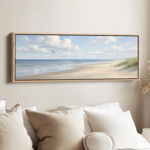 May include: A rectangular framed painting of a beach scene. The artwork shows a sandy beach, the sea, and a blue sky with clouds. Several seagulls are flying. The frame is made of light-coloured wood.