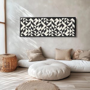 Puede incluir: Una pieza de arte mural rectangular que presenta un patr&oacute;n geom&eacute;trico repetitivo de tri&aacute;ngulos y cuadrados en negro y blanco roto. La obra est&aacute; encerrada en un marco negro fino y muestra un dise&ntilde;o sim&eacute;trico de alto contraste en toda su superficie.