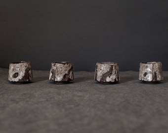 May include: Four small, ceramic cups with a white glaze and brown speckles. The cups are arranged in a row on a gray surface.
