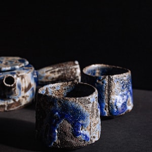 Könnte beinhalten: Ein Set aus drei Keramik-Teetassen und einer Teekanne, alle mit einer blauen und weißen Glasur. Die Tassen und die Teekanne haben ein rustikales, handgemachtes Aussehen.