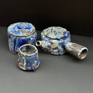 Peut inclure: Un service à thé en céramique bleu et brun avec une théière, un récipient avec couvercle et une petite tasse.