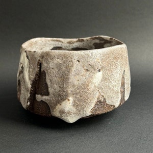 May include: A ceramic bowl with a textured, irregular surface. The bowl is a mottled brown and white colour, with a rough, uneven glaze.