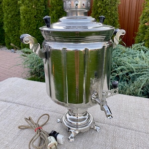 May include: A silver electric samovar with a black cord and plug. The samovar has a spout and two handles. It has a decorative top with a star design.