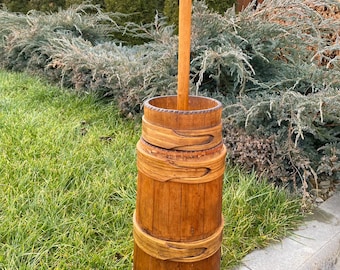 May include: A wooden butter churn with a long wooden handle. The churn is made of multiple sections and has a natural wood finish.