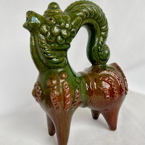 Könnte beinhalten: Keramikfigur einer Fabelwesen, mit grünem Kopf und Oberkörper und braunem Unterkörper. Die Figur hat einen geschwungenen, verzierten Rücken und steht auf vier Beinen. Die Glasur hat ein glänzendes Finish.