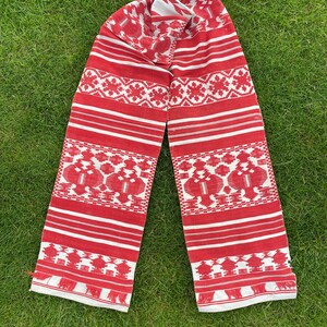 May include: A red and white woven scarf with a geometric pattern. The scarf is folded in half and laid out on a green grassy surface.