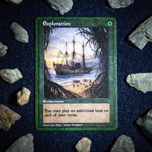 Può includere: Una carta verde con la parola "Exploration" in alto. La carta presenta un'illustrazione di una nave su una spiaggia. Il testo sulla carta recita: "Puoi giocare una terra aggiuntiva in ognuno dei tuoi turni."