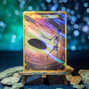 May include: A rectangular trading card titled Warp featuring a holographic illustration of a human skeleton reaching toward a dark oval void surrounded by swirling cosmic colors of purple, orange, and blue, set within a decorative gold border.