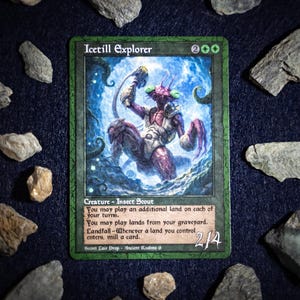 Peut inclure: Une carte Magic: The Gathering, "Icetill Explorer", présente une créature insectoïde violette avec une armure blanche. La carte a une bordure verte et du texte décrivant ses capacités. La carte est entourée de roches grises sur une surface bleu foncé.