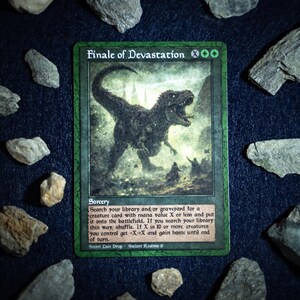 May include: A green card labelled "Finale of Devastation" with a dinosaur illustration. The card is surrounded by various grey and brown rocks on a dark blue surface. The card text describes a sorcery spell.
