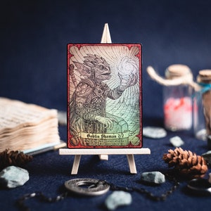 Op de afbeelding: Een fantasy trading card met een illustratie van een goblin-sjaman. De kaart is rood, groen en wit met een zwarte rand. De tekst op de kaart luidt "Goblin-sjaman 2/2 Telkens wanneer dit wezen aanvalt, creëer een schat-token."
