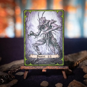 May include: A fantasy art card featuring a detailed illustration of an insectoid creature. The card has a green and black border with the text "Insect 1/1" at the bottom. The creature is depicted in shades of gray and purple, with sharp claws and a menacing expression.