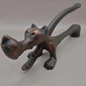 Può includere: Un schiaccianoci vintage color bronzo a forma di lupo con la bocca aperta e una lunga coda. Lo schiaccianoci è in metallo e ha un design dettagliato.