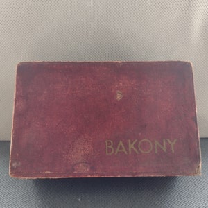 Pode incluir: Uma caixa bordô com letras douradas que dizem "BAKONY".