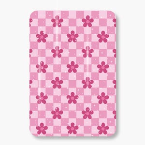 Può includere: Un oggetto rettangolare rosa con un motivo ripetuto di fiori rosa su uno sfondo a scacchi. I fiori hanno cinque petali e sono uniformemente distanziati. Piccoli accenti bianchi a forma di stella sono sparsi in tutto il design.