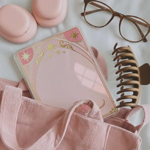 Può includere: Una custodia per telefono rosa con un design dorato e rosa con stelle ed elementi floreali è parzialmente visibile all'interno di una borsa tote di velluto a coste rosa. Altri oggetti includono una pinza per capelli marrone, occhiali e auricolari wireless rosa.