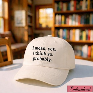 Może przedstawiać: Kremowa czapka bejsbolówka z wyhaftowanym tekstem "i mean, yes. i think so. probably." Czapka ma zakrzywiony daszek i guzik na górze. Słowo "Embroidered" znajduje się w różowym prostokącie w prawym dolnym rogu.