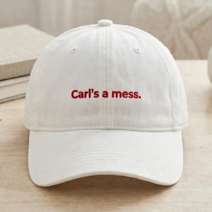 Puede incluir: Gorra de béisbol blanca con visera curva y correa ajustable. La gorra presenta el texto bordado "Carl's a mess" en hilo rojo en la parte delantera. Hecha de tela suave y duradera.