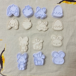 May include: A collection of bunny and carrot-shaped cookie cutters in various designs. The cutters are in shades of white and light blue, perfect for Easter-themed baking. The designs include bunny faces, carrots, and Easter eggs.