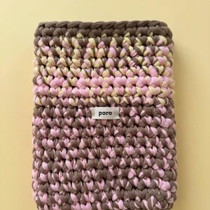 Könnte beinhalten: Eine rechteckige, handgehäkelte Tasche in Braun-, Rosa- und Gelbtönen. Die Tasche hat ein strukturiertes Stichmuster und ein kleines weißes Etikett mit dem Wort "paro". Die Tasche wird wahrscheinlich zum Tragen von Gegenständen verwendet.