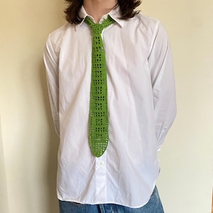 May include: A white button-down shirt with a green crocheted tie. The tie has a square pattern.