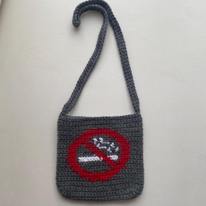 Könnte beinhalten: Eine graue gehäkelte Umhängetasche mit einem roten Kreis und einem weißen Nichtraucher-Symbol.