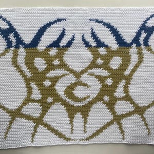 Puede incluir: Una manta de ganchillo blanca con un diseño de dos grandes formas abstractas estilizadas en verde oliva y azul marino.