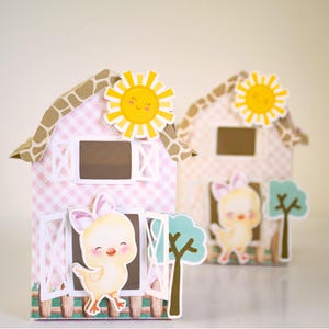 May include: Two pink and brown barn-shaped boxes with a yellow sun and a yellow chick peeking out of the window. The boxes are decorated with a gingham pattern and have a white picket fence.