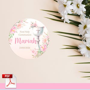 Puede incluir: Una pegatina redonda blanca con flores rosas y un cáliz plateado con una cruz en la parte superior. El texto en la pegatina dice "First Holy Communion Mariah 23/05/2026".