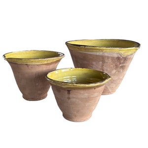 May include: Three terracotta bowls with yellow glazed rims. The bowls are nested together, with the largest bowl at the bottom and the smallest bowl at the top.
