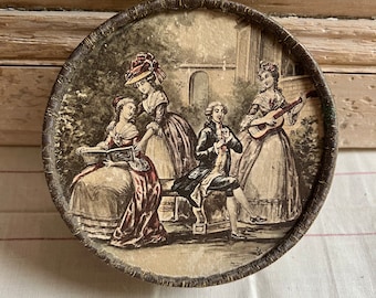 May include: A round, brown, cardboard box with a vintage design. The lid features a scene of four people in a garden setting. Two women are dressed in long gowns, one is reading a book, and the other is holding a fan. A man is playing a flute, and another woman is playing a guitar.